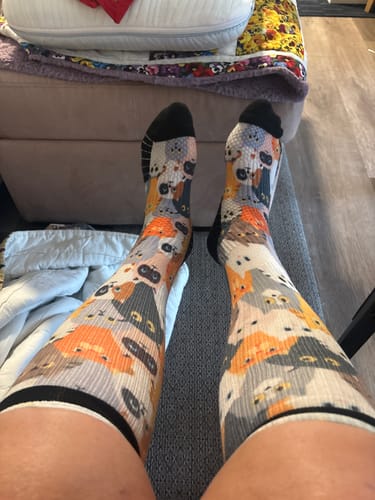 Customer's legs wearing compression socks featuring a multi-colored cat print pattern.