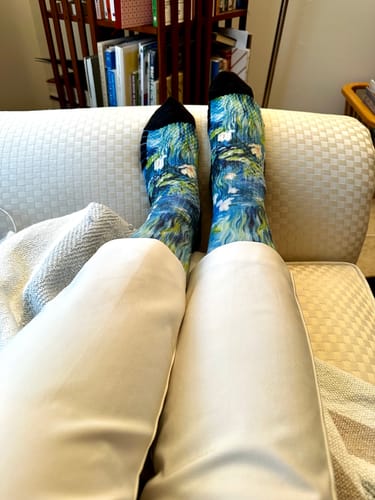 A reviewer relaxing on a couch, wearing the patterned Water Lily Compression Socks with white pants.